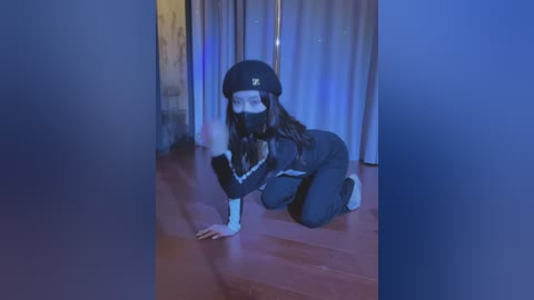 Media: A video of a person with a long beard, wearing a black beret, black mask, and dark clothing, crawling on a wooden floor in a dimly lit room with blue curtains and a partly open door.