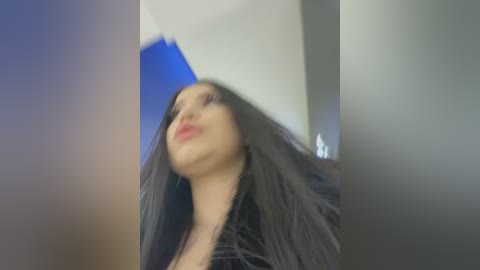 Media: Video of a woman with long black hair, wearing a black jacket, with a large white sheet draped over her head, creating a surreal, dream-like effect. The background is blurred.