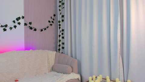 Media: A cozy, softly lit room with a beige couch, white fur blanket, and sheer curtains with green ivy patterns. Pink and purple lights cast a gentle glow, creating a serene ambiance.