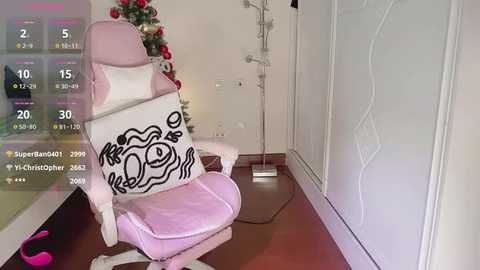 Media: Video of a pastel pink gaming chair with a cartoon character pillow in a minimalist, white-walled room, featuring medical equipment and a Christmas tree.