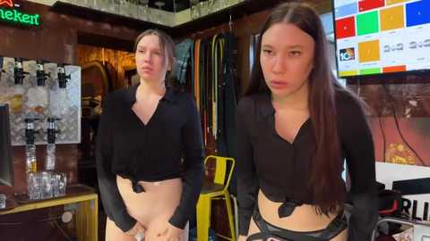 Media: Video of two young women with long brown hair in black crop tops and black panties in a dimly lit bar.