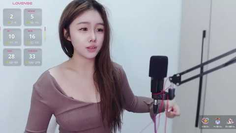 Media: Video of an Asian woman with long brown hair, wearing a beige top, holding a microphone, against a white background with a calendar.