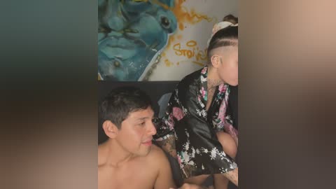 Media: Video of a shirtless, tattooed man kissing a woman with a floral kimono, set against a colorful abstract painting background.