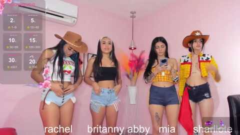 Media: Video of four women in western attire, standing against a pink wall, wearing cowboy hats, shorts, and crop tops.