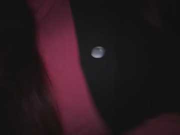 A video shows a blurred, dark silhouette of a person with a pink object in the foreground, likely a piece of clothing or accessory, against a black background.