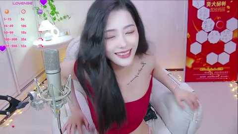 Media: Video of an Asian woman with long black hair, wearing a red crop top, sitting on a white chair, smiling while singing into a microphone, surrounded by festive decorations and a red poster.