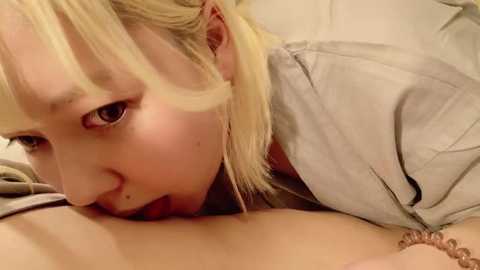 Media: A close-up video of a young Asian woman with straight blonde hair, fair skin, and brown eyes, performing oral sex on a male partner.