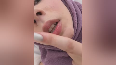 Media: Video of a close-up of a woman's face with fair skin, full lips, and a purple towel covering her head. Her fingernails are painted white, and her eyes are partially visible.