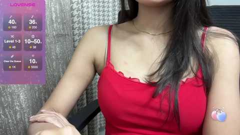 Media: Video of a young Asian woman with long black hair, wearing a red spaghetti-strap top, sitting indoors with a colorful health app screen in the background.