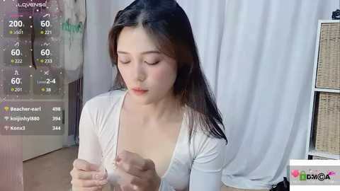 Media: A video of an Asian woman with long black hair, wearing a white top, playing with a phone in a room with white curtains and a wicker basket.