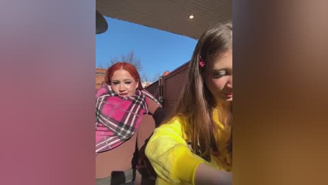 Media: Video of two young girls, one with red hair, the other with brown hair, both wearing plaid shirts, riding on a red scooter outdoors under a clear blue sky.