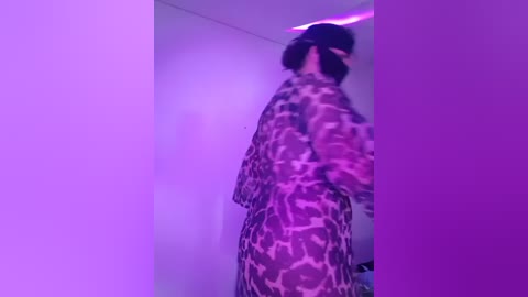 Media: A video of a woman with dark hair wearing a leopard print robe, taken from behind, in a dimly lit room with purple lighting.