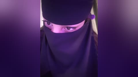 Media: Video of a person with a black headscarf and sunglasses, eyes peering out, against a purple gradient background, creating a mysterious, intense atmosphere.