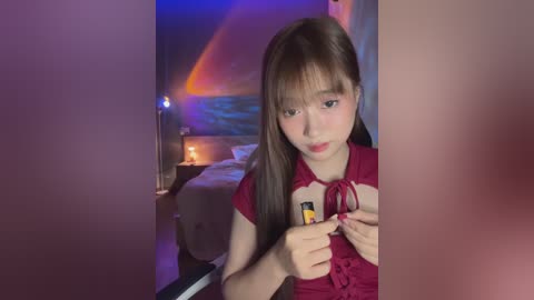 Media: A video of a young Asian woman with long brown hair, wearing a red lace top, holding a lighter, indoors with dim lighting and a bed in the background.