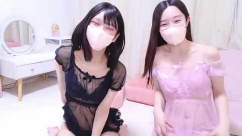 Media: Video of two Asian women in matching light pink lace lingerie, face masks, and black sheer mesh tops, sitting on a bed. Background includes a white vanity and round mirror.