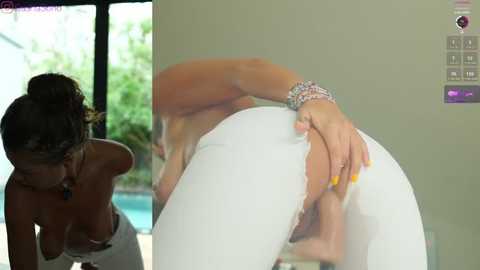 Media: Video of a nude woman with light brown skin, bent over, wearing tight white pants, revealing her vagina, with a bracelet on her wrist. Background shows a sunlit room with a pool.