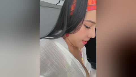 Media: Video of a young woman with long black hair, wearing a red bandana, and a white shirt, standing in a dimly lit room.