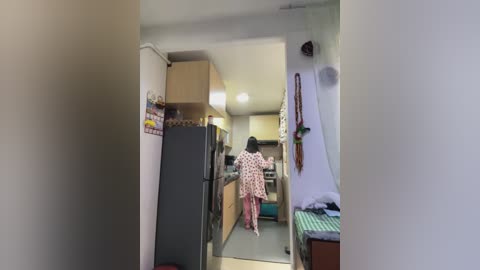 Media: Video of a narrow, cluttered hallway with a person in a polka-dot robe walking away, leading to a small kitchen with appliances and hanging items on the walls.