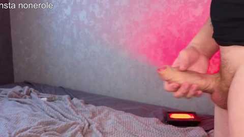 Media: A video shows a man with a flaccid penis, holding a vibrator against his skin, in a dimly lit room with a pink and blue wall.