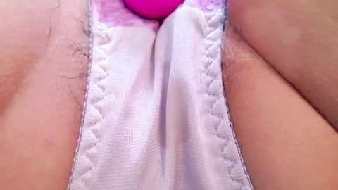 Media: Close-up video of a woman's crotch, showing a white thong with a pink clitoral stimulator, visible pubic hair, and light skin.