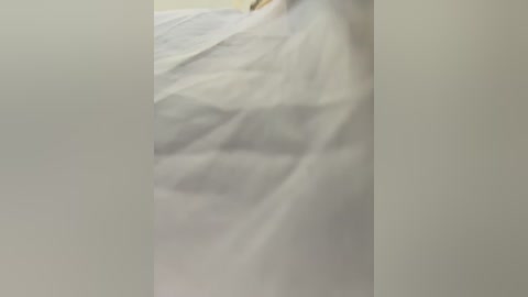 Media: A blurry video of a person's legs and lower torso partially covered by a white sheet, with a plain beige wall in the background.