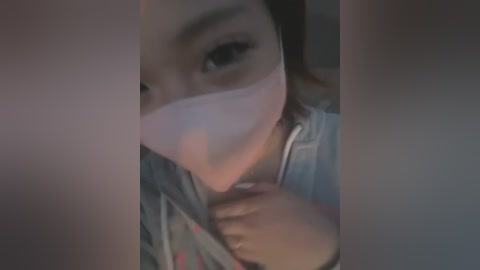 Media: Video of a woman with light skin and dark hair wearing a pink mask, partially covering her face, holding a phone in her right hand.