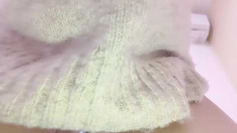 Media: Video of a fluffy, pale green, textured fabric resembling a ball of yarn, with soft, flowing strands, set against a blurred, light pink background.