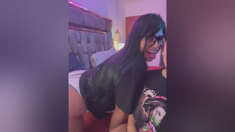 Media: Video of a young woman with long black hair and glasses, wearing a black t-shirt and red panties, leaning over a bed in a dimly lit room with purple lighting.