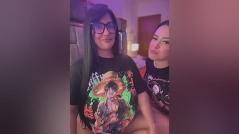 Media: Video of two women, one with long black hair and glasses, wearing a \"Pirate King\" t-shirt, the other with short brown hair, both indoors with purple lighting.