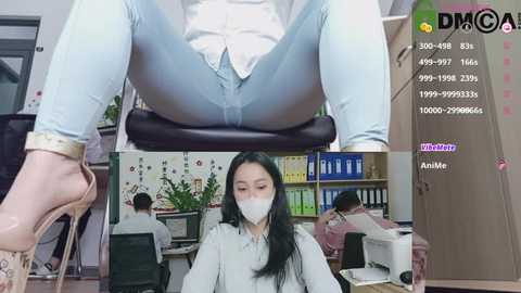 Media: A video of a woman in a white blouse and light jeans seated at a desk, surrounded by office supplies and coworkers.