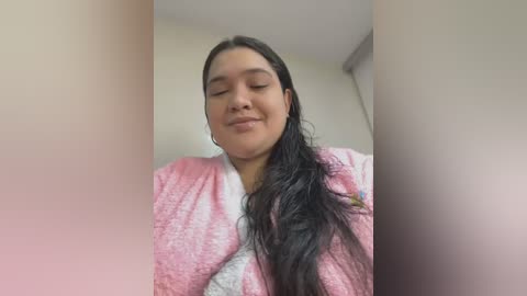 Media: A video of a young Latina woman with long, dark hair, wearing a pink bathrobe, smiling softly with closed eyes in a softly lit room.