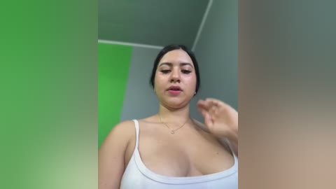 Media: Video of a curvy Latina woman with medium skin tone, black hair pulled back, wearing a white tank top that reveals ample cleavage, captured from below.