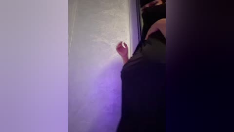 Media: A video captures a person in black clothing reaching out to a white wall with a soft, purple light illuminating the scene, creating a mysterious, slightly blurred atmosphere.