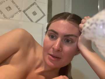 Media: Video of a young, fair-skinned woman with straight brown hair, leaning against a tiled wall, applying soap to her face with a sponge.