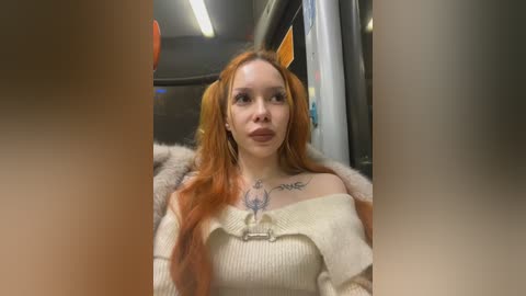 Media: Video of a fair-skinned woman with long, fiery red hair styled in twin ponytails. She's wearing a cream-colored off-shoulder sweater, a necklace, and a furry collar. She sits inside a dimly lit subway car, with a blurred background.