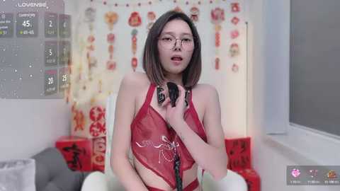 Media: A video of an Asian woman with glasses, medium-length dark hair, wearing a red lace lingerie set, singing into a microphone, in a festive room with holiday decorations.