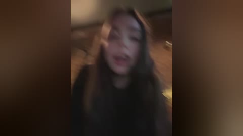 Media: Blurry video of a young Asian woman with long, straight hair, wearing a black top, taken indoors in dim lighting. Her expression is unclear due to the low resolution.