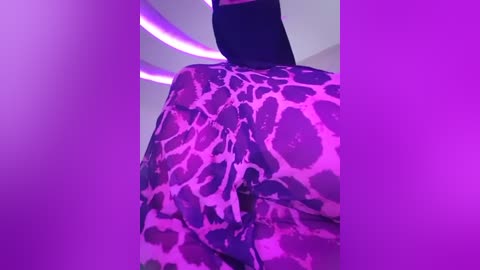 Media: A video of a person wearing a leopard-print jacket, standing in a room lit with purple lights, creating a vibrant, night club-like atmosphere. The jacket is vibrant and patterned, contrasting with the dark background.