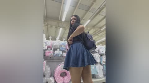 Media: Video of a young woman with long black hair, wearing a dark sleeveless top and a short blue skirt, shopping in a brightly lit toy store.