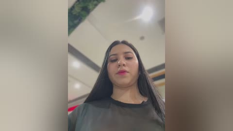 Media: A video of a Latina woman with long black hair, wearing a black leather jacket, standing in a modern indoor space with a green plant and white ceiling.