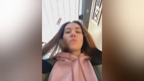 Media: A blurry video of a young woman with long brown hair, wearing a pink hoodie, captured from an angled perspective.