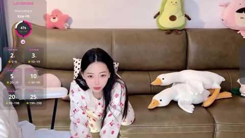 Media: A video of an Asian woman in a white pajama set with red hearts, leaning over a beige sofa, surrounded by plush toys including a duck.