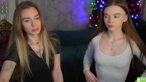 Media: A video shows two young women with long blonde hair, one in a black top, the other in a light grey tank, standing indoors with a festive, multicolored backdrop.