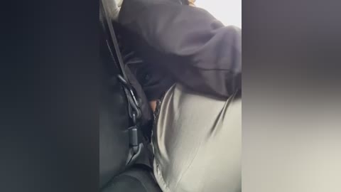 Media: Video of a person wearing a black jacket and light-colored pants, leaning against a dark vehicle interior. The person\u2019s face is obscured, and the lighting is dim.