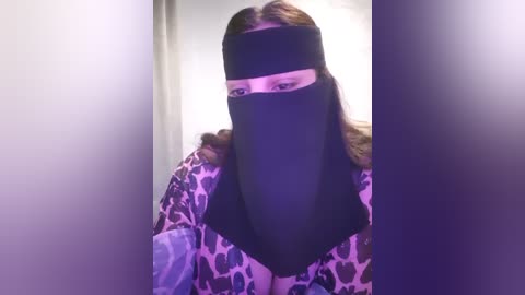 Media: Video of a person with long brown hair, wearing a black face mask and leopard-print jacket, standing in a dimly lit hallway.