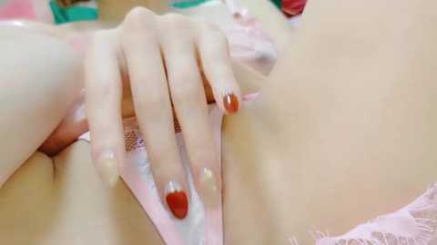 Media: A video of a light-skinned hand with red and gold nail polish, gently touching a light pink satin bra, creating a soft and sensual ambiance.