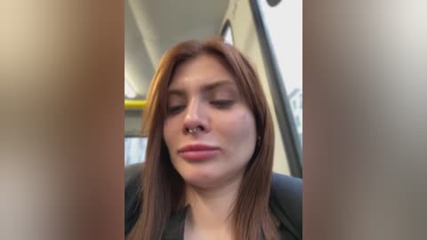 Media: A video of a woman with straight, reddish-brown hair and light skin, wearing a nose ring and closed eyes, seated in a dimly lit bus.