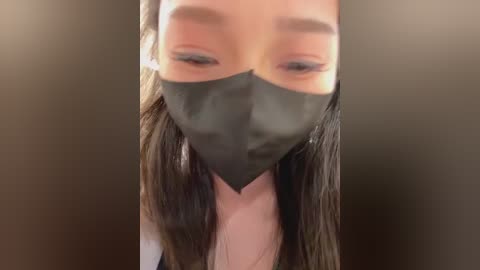 Media: Video of a woman with long, wet, dark hair, wearing a black face mask, focusing on her eyes and mouth, blurred background.