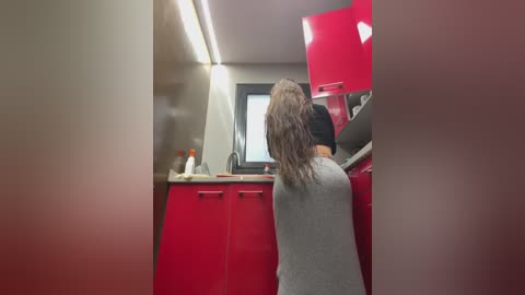 Media: A video captures a person with wet hair, wearing a black blindfold, standing in a modern kitchen with red cabinets and a stainless-steel sink, under bright fluorescent lighting.