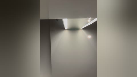 Media: A video of a minimalist, modern interior featuring a stark white ceiling with recessed lighting, casting soft shadows on the smooth, beige walls. The image has a soft focus, creating a serene and calm atmosphere.